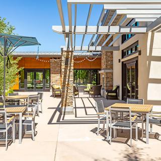 A modern outdoor patio area with tables, chairs, and a pergola on a sunny day.