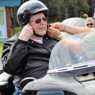 A person is preparing to ride a motorcycle, fastening their helmet outdoors.
