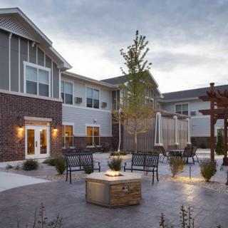 A cozy outdoor patio with seating around a fire pit in front of a modern building at dusk.