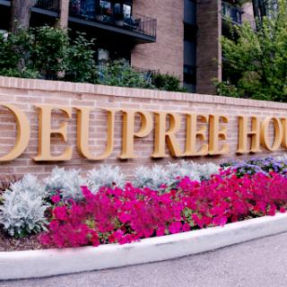 Entrance sign of Deupree House surrounded by colorful flowers.