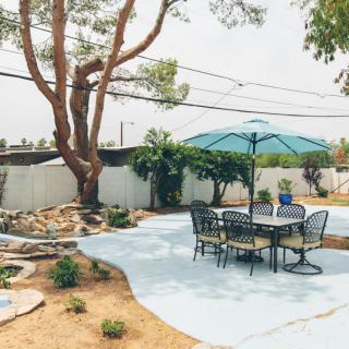 A serene backyard patio with a table, chairs, and umbrella set against a landscaped garden.