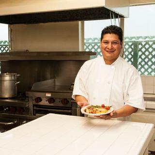 A chef presenting a dish in a professional kitchen.