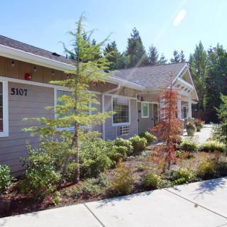 A residential building with landscaped gardens and trees on a sunny day.