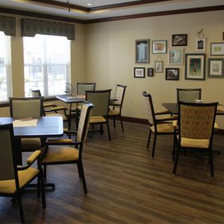 A cozy dining area with multiple tables and chairs, decorated with wall art and large windows for natural light.