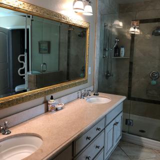 A modern bathroom with a double sink, large mirror, and glass-enclosed shower.