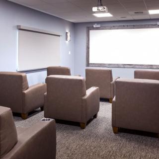 A cozy conference room with comfortable seating and a large projector screen for presentations.