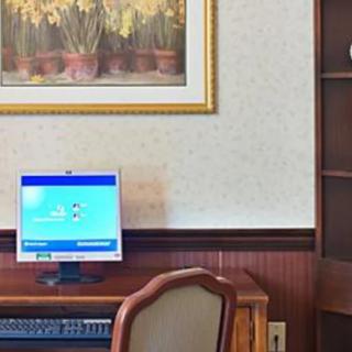 An office setup with a computer on a wooden desk, accompanied by a chair and a decorative painting on the wall.