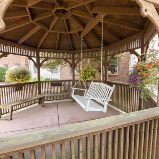A wooden gazebo with a white swing and hanging plants.