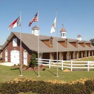 A row of flags in front of a barn with a white fence.