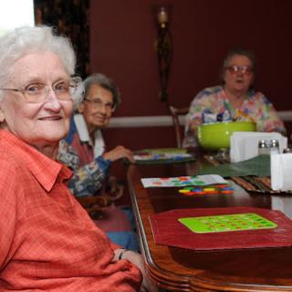 A warm moment captured at a gathering of elderly women enjoying each other's company around the dining table.