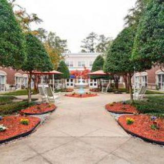 A beautifully landscaped garden with a symmetrical design featuring trimmed trees and colorful flowerbeds lining a central pathway.