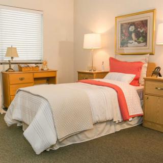 A cozy bedroom with a neatly made bed, surrounded by wooden furniture and soft lighting.
