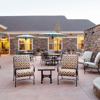 A cozy outdoor patio area with comfortable seating and tables, surrounded by a stone building in the evening light.