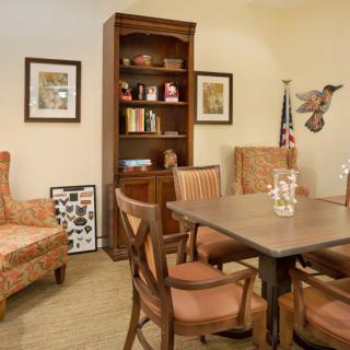 A cozy office meeting area with a wooden table, chairs, and a bookshelf adorned with various decorations.