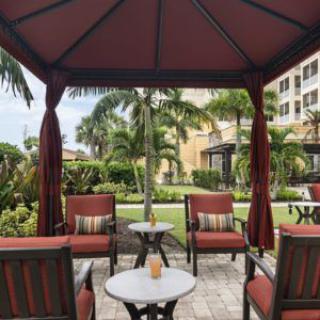 A cozy outdoor gazebo area with seating, surrounded by lush gardens and palm trees.