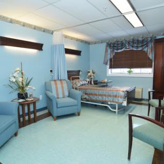 A well-furnished hospital patient room featuring a bed, seating area, and calming blue decor.