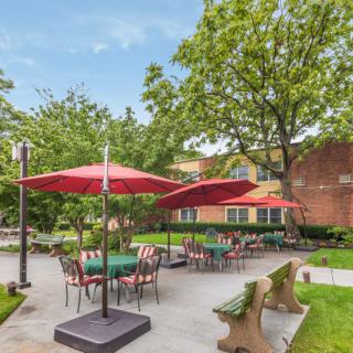 An inviting outdoor patio area with tables, chairs, and umbrellas surrounded by greenery.