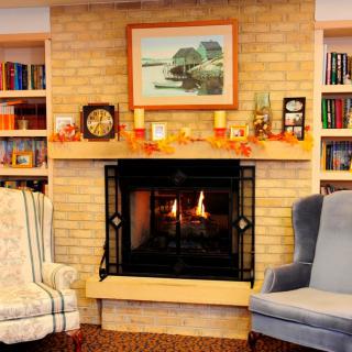 A cozy living room with a fireplace, flanked by armchairs and bookshelves.