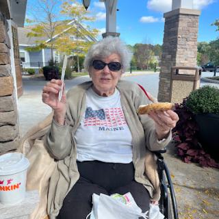 An elderly woman enjoying a snack outdoors on a sunny day.