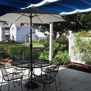A cozy outdoor seating area with a table and chairs under an umbrella, surrounded by greenery.
