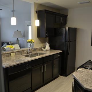A modern kitchen with dark cabinets, granite countertops, and pendant lighting.