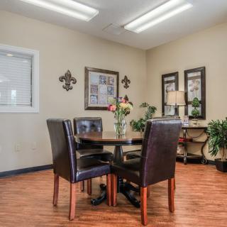 A cozy office meeting room with a round table, four chairs, and decorative elements such as plants and artwork.