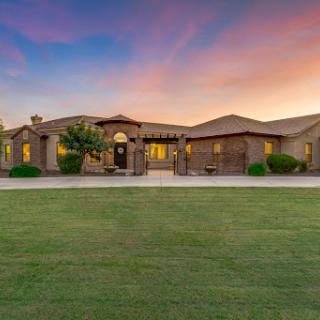 A beautiful home illuminated by the glow of a sunset, surrounded by lush green grass.