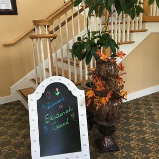 A welcoming autumn-themed sign next to a staircase with plants and seasonal decorations.