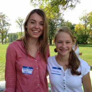 Two people smiling outdoors with name tags, enjoying a sunny day.