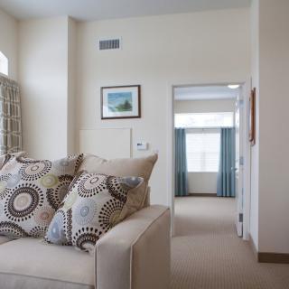 A cozy living room featuring a sofa with decorative pillows, leading to another room through an open doorway.