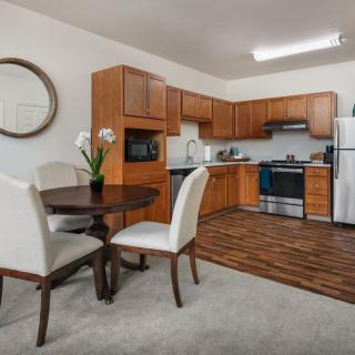 A modern kitchen and dining area featuring wooden cabinets, a round dining table with chairs, and standard kitchen appliances.