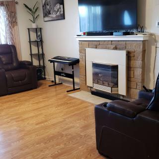 A cozy living room with recliner chairs, a television above a fireplace, and hardwood flooring.