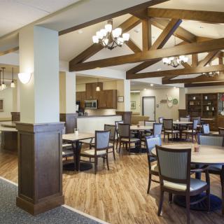 A spacious dining area with wooden beams, featuring round tables and chairs, illuminated by elegant chandeliers.