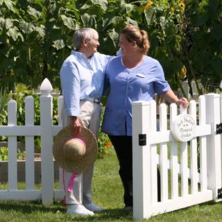 Two women enjoying time together in a garden by a white picket fence.