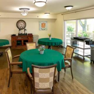 A cozy dining area with round tables covered in green tablecloths, wooden chairs, and a wooden floor.