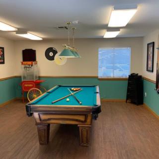 A cozy billiards room featuring a pool table with cue sticks and balls, an arcade game, and decorative posters on the walls.