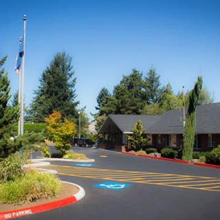 A well-maintained building surrounded by trees with a driveway and flagpole in the foreground.