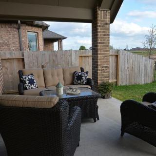 A cozy outdoor patio setup with furniture, including a couch and chairs, next to a wooden fence and brick house.