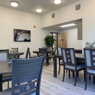 A modern dining area with several tables and chairs, decorated with plants and contemporary lighting.