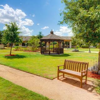 A tranquil park scene featuring a wooden bench along a pathway, with a gazebo and lush greenery.