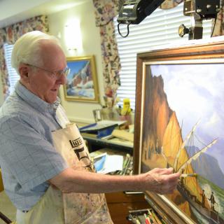 An artist is working on a landscape painting in his art studio.