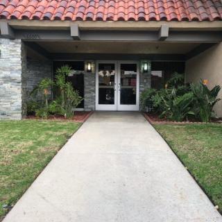 A building entrance with a concrete pathway and surrounding plants.