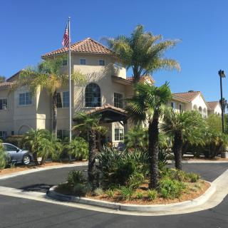 A residential building surrounded by palm trees and landscaping, with an American flag displayed at the entrance.