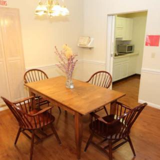 A cozy dining room with a wooden table and chairs, featuring a chandelier and an adjacent kitchen.