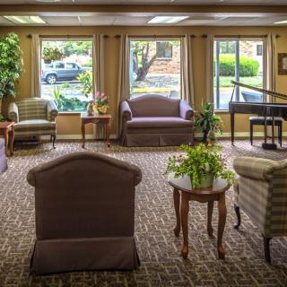 A cozy living room with comfortable seating and a piano by large windows.