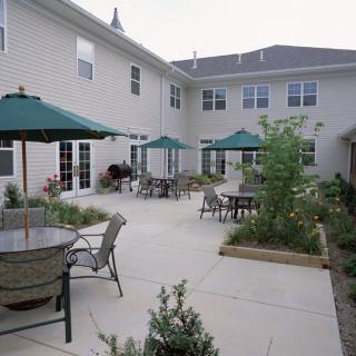 A spacious patio area with tables, chairs, and green umbrellas outside a residential building.