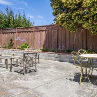 A sunny patio with outdoor seating surrounded by a wooden fence and greenery.