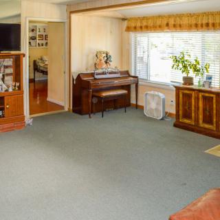 A cozy living room with a piano and television, featuring a large window and indoor plant.