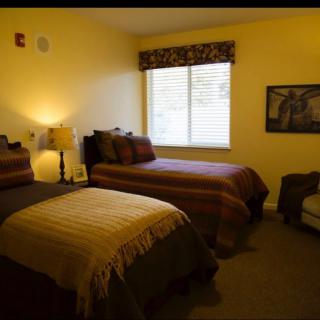 A cozy bedroom with twin beds, a lamp, and an armchair near the window.