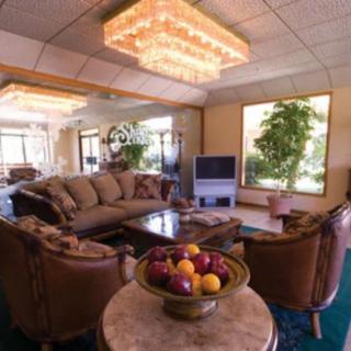 A cozy living room with a comfortable sofa, chairs, and a coffee table, featuring a chandelier and large windows letting in natural light.